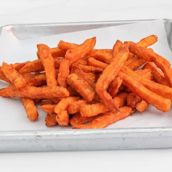 A pile of orange sweet potato fries in a metal tray with white paper.