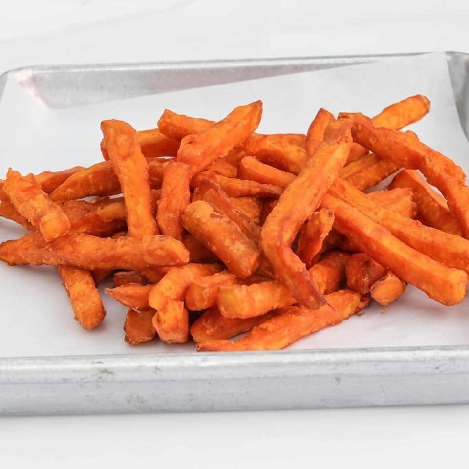A pile of orange sweet potato fries in a metal tray with white paper.