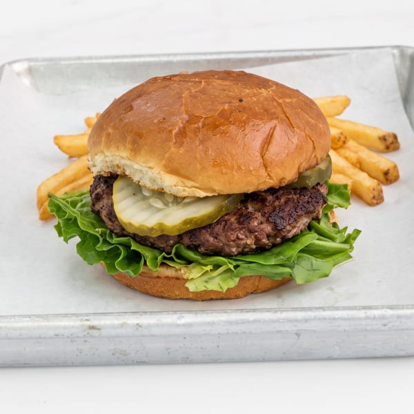 Burger with lettuce, pickles, and fries on a metal tray.